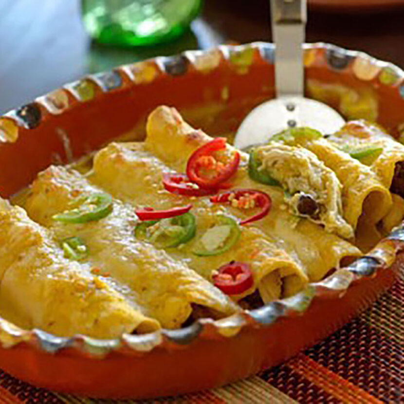 An image of prepared Butternut Squash and Salsa Verde Enchiladas made with Pacific Foods® Organic Creamy Butternut Squash Soup, chicken, salsa verde, black beans, corn tortillas, pepper Jack cheese and sour cream.