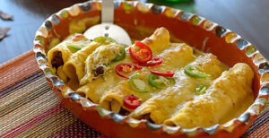 An image of prepared Butternut Squash and Salsa Verde Enchiladas made with Pacific Foods® Organic Creamy Butternut Squash Soup, chicken, salsa verde, black beans, corn tortillas, pepper Jack cheese and sour cream.