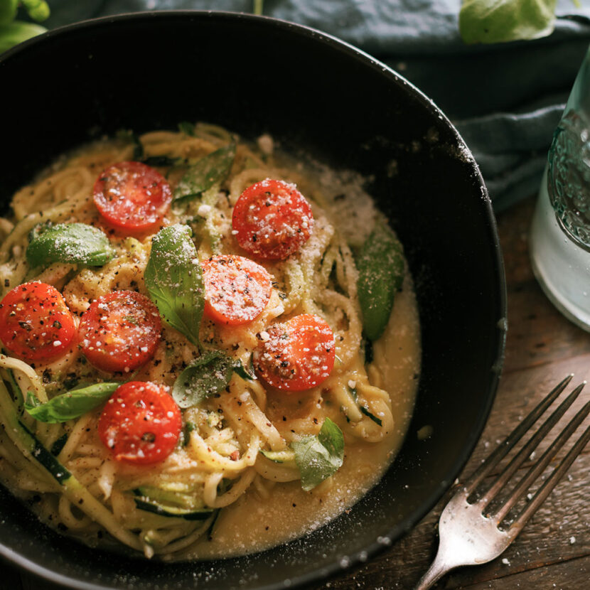 An image of prepared Carrot Ginger Cashew Alfredo Sauce for Zoodles made with Pacific Foods® Organic Almond Original Beverage, Pacific Foods® Organic Cashew Carrot Ginger Soup, zucchini noodles, cherry tomatoes and basil.