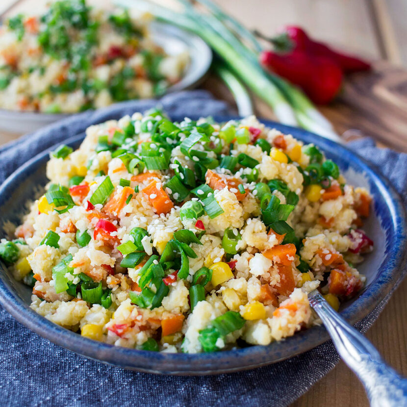 An image of prepared Cauliflower Fried Rice made with cauliflower florets, carrots, corn, peas, Pacific Foods® Unsalted Chicken Stock, eggs, green onion, soy sauces and sesame seeds.