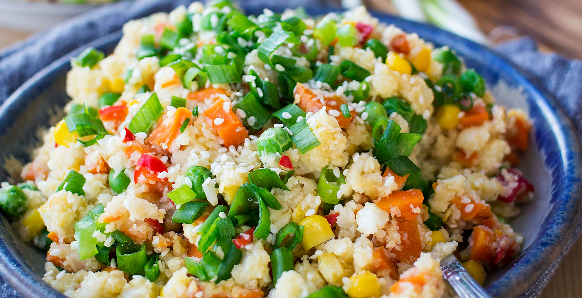 An image of prepared Cauliflower Fried Rice made with cauliflower florets, carrots, corn, peas, Pacific Foods® Unsalted Chicken Stock, eggs, green onion, soy sauces and sesame seeds.