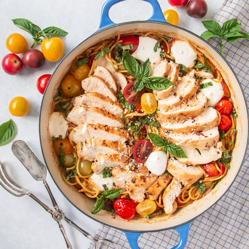 An image of prepared Chicken Caprese One Pot Pasta made with chicken, garlic, cherry tomatoes, white wine, spaghetti, Pacific Foods® Organic Chicken Stock, Parmesan cheese, mozzarella cheese and basil.