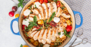 An image of prepared Chicken Caprese One Pot Pasta made with chicken, garlic, cherry tomatoes, white wine, spaghetti, Pacific Foods® Organic Chicken Stock, Parmesan cheese, mozzarella cheese and basil.