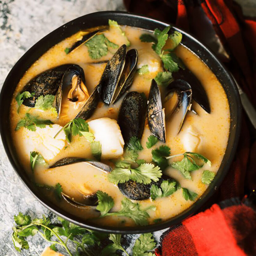 An image of prepared Coconut Curry Soup with Mussels and Scallops made with Pacific Foods® Organic Vegetable Broth, Pacific Foods® Organic Coconut Beverage, mussels, scallops and cilantro.