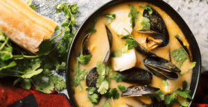 An image of prepared Coconut Curry Soup with Mussels and Scallops made with Pacific Foods® Organic Vegetable Broth, Pacific Foods® Organic Coconut Beverage, mussels, scallops and cilantro.