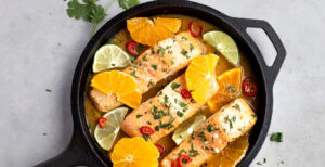 An image of prepared Coconut Citrus Poached Salmon made with oranges, limes, Pacific Foods® Organic Coconut Unsweetened Plant-Based Beverage, Pacific Foods® Organic Low Sodium Vegetable Broth, salmon and cilantro.