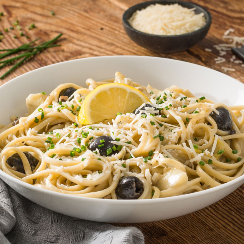 An image of prepared Creamy Mushroom-Artichoke Pasta made with linguine, Pacific Foods® Organic Cream of Mushroom Condensed Soup, artichoke hearts, black olives, chives and Parmesan cheese.