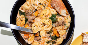 An image of prepared Creamy Sausage & Tortellini Soup made with Italian pork sausage, onion, carrots, garlic, Italian seasoning, Pacific Foods® Organic Free Range Chicken Broth, cream, tomato paste, cheese tortellini and kale.