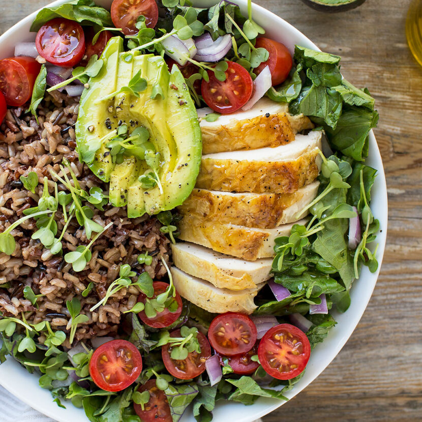 An image of prepared Grilled Chicken and Wild Rice Bone Broth Bowl made with Pacific Foods® Unsalted Organic Chicken Bone Broth, wild rice, chicken, romaine, cherry tomatoes, mixed micro greens, avocado, red onion and balsamic vinegar.