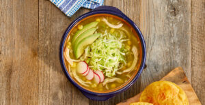 An image of prepared Instant Pot® Posole Verde made with tomatillos, garlic, Pacific Foods® Organic Free Range Low Sodium Chicken Broth, rotisserie chicken, hominy, avocado and radish.