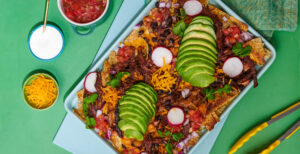 An image of prepared Instant Pot® Shredded Beef Nachos made with Pacific Foods® Organic Beef Broth, chuck roast, tortilla chips, red onion, Cheddar cheese, pico de gallo, black beans, pinto beans, cilantro, radish and avocado.