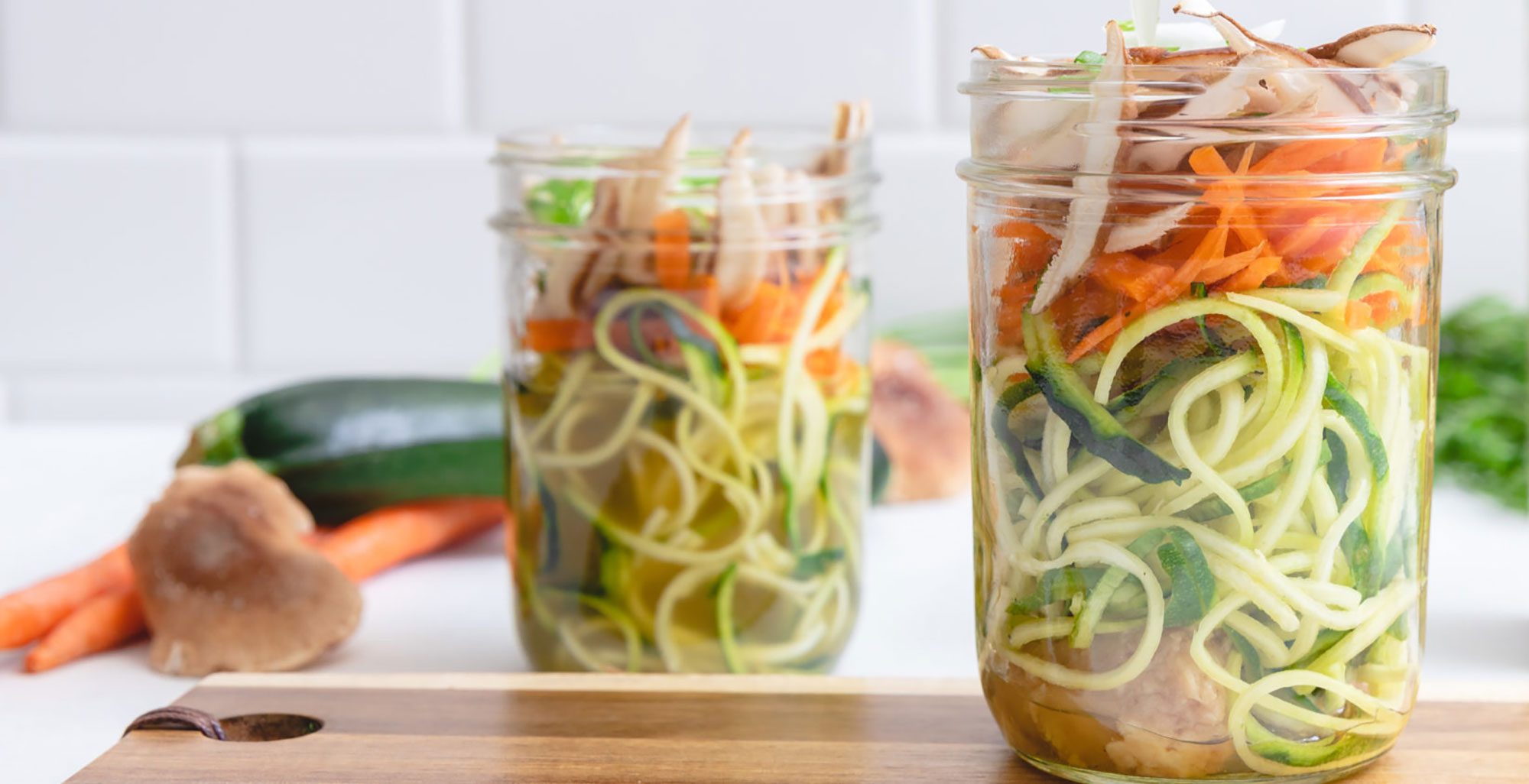 An image of prepared Mason Jar Miso Zoodle Soup made with zucchini noodles, green onion, shiitake mushrooms, carrot, white miso, sesame oil and Pacific Foods® Organic Free Range Chicken Broth.