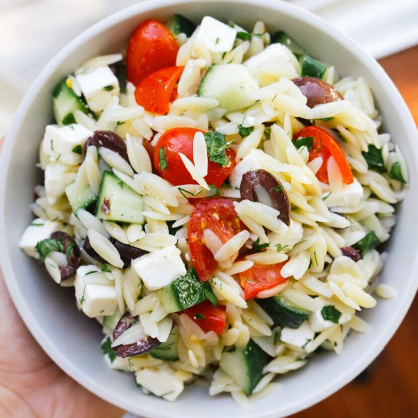 An image of prepared Mediterranean Orzo Salad made with Pacific Foods® Organic Low Sodium Vegetable Broth, orzo pasta, feta cheese, cherry tomatoes, cucumber, kalamata olives, parsley and dill.