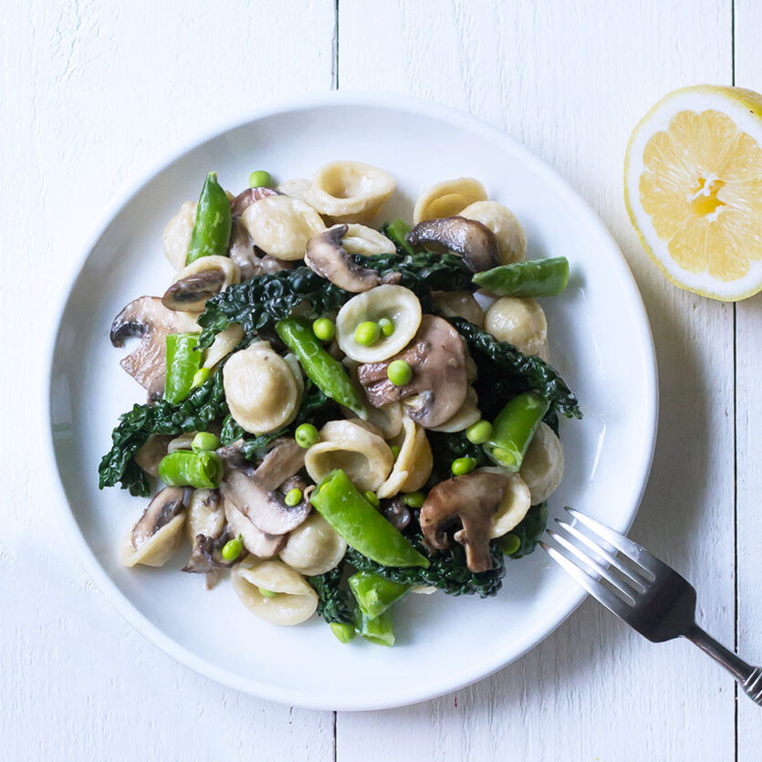 An image of prepared Mushroom Pasta with Spring Peas in Cream Sauce made with Pacific Foods® Mushroom Broth, spring peas, orecchiette pasta, kale, cremini mushrooms, Pacific Foods® Organic Almond Original Plant-Based Beverage and garlic.