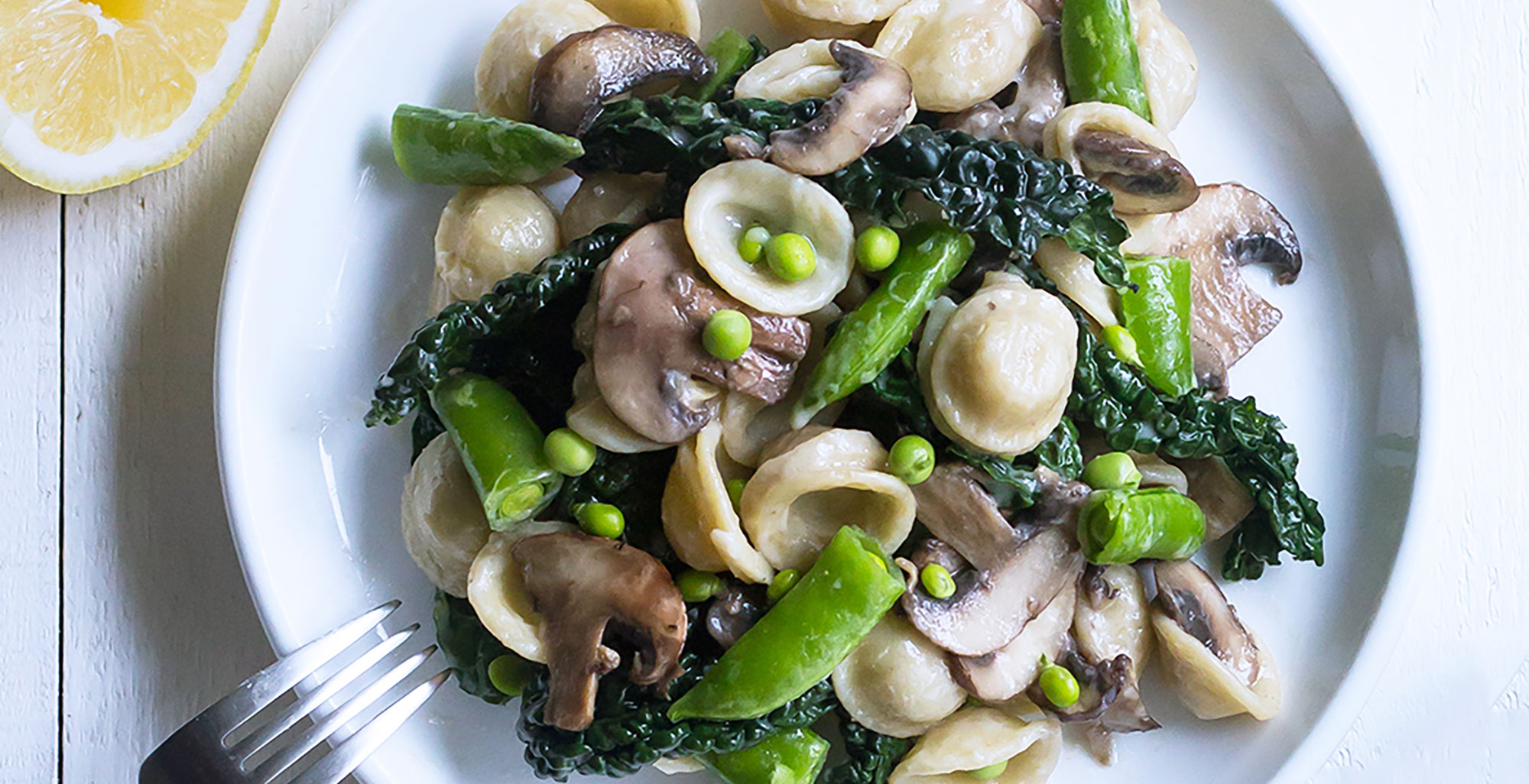 An image of prepared Mushroom Pasta with Spring Peas in Cream Sauce made with Pacific Foods® Mushroom Broth, spring peas, orecchiette pasta, kale, cremini mushrooms, Pacific Foods® Organic Almond Original Plant-Based Beverage and garlic.