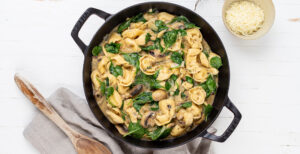 An image of prepared One-Pot Creamy Mushroom Tortellini made with mushrooms, thyme, Pacific Foods™ Organic Free Range Chicken Broth, Pacific Foods™ Organic Cream of Mushroom Condensed Soup, cream, tortellini, baby spinach and Parmesan.