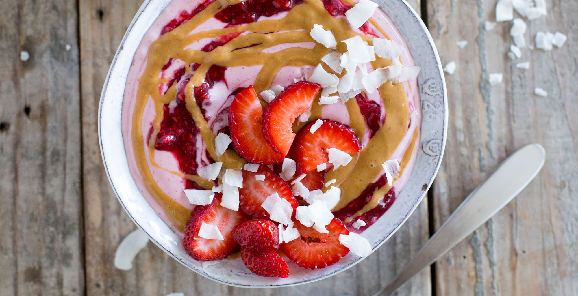 An image of prepared Peanut Butter and Jelly Smoothie Bowl made with strawberries, banana, Pacific Foods® Organic Coconut Unsweetened Original Beverage, peanut butter, strawberry jelly and coconut flakes.
