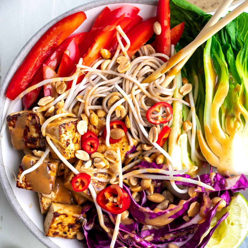 An image of prepared Peanut Tofu Noodle Bowl made with tofu, honey, peanut butter, sesame oil, tamari, Pacific Foods® Organic Mushroom Broth, Japanese soba noodles, bok choy, bean sprouts, red bell pepper, red cabbage, red chili pepper, peanuts and limes.