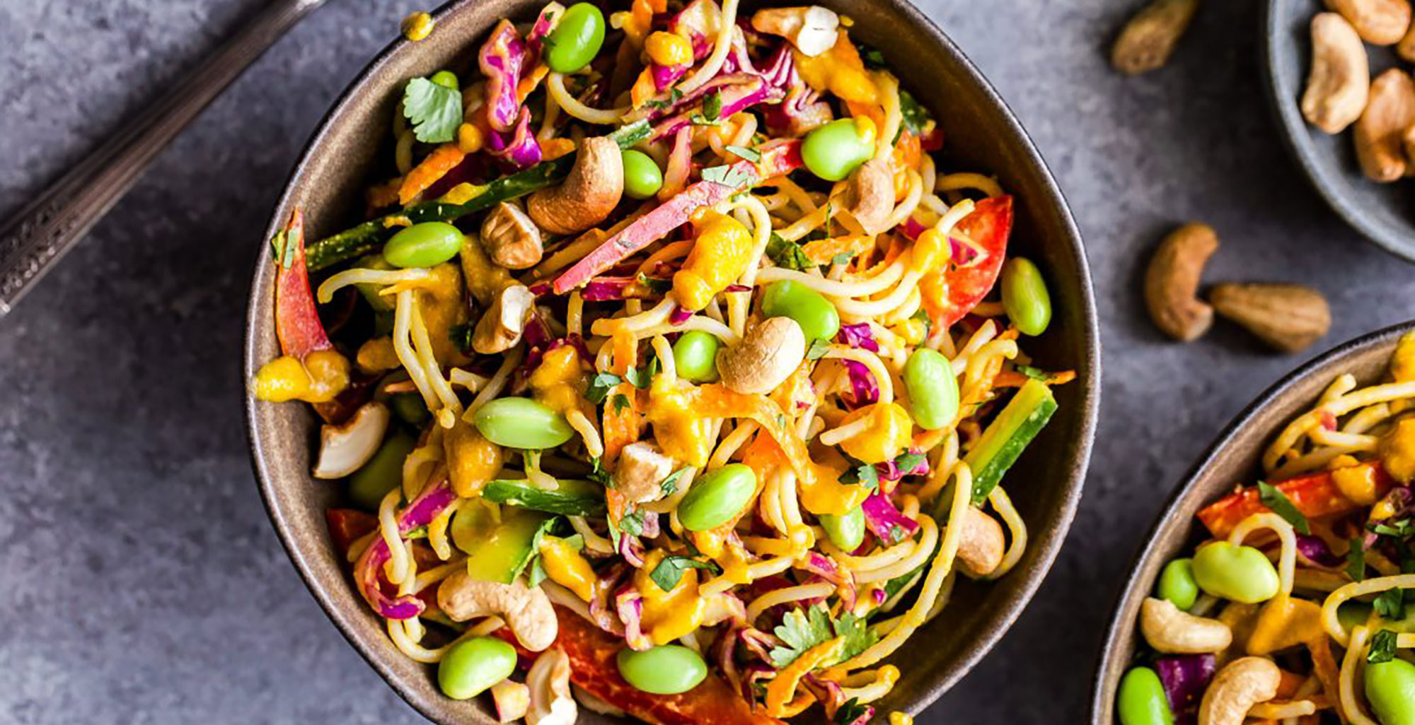 An image of prepared Thai Noodle Salad with Cashew Carrot Ginger Sauce made with Pacific Foods® Organic Cashew Carrot Ginger Soup, brown rice noodles, cucumber, bell pepper, carrot, green onion, edamame and cilantro.