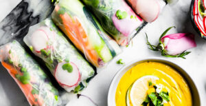 An image of prepared Vegan Spring Rolls with Ginger Curry Dipping Sauce made with Pacific Foods® Organic Cashew Carrot Ginger Soup, cashews, cilantro, rice paper wrapper, carrot, cucumber, zucchini, radish, bean sprouts, cabbage, green onion and cilantro.