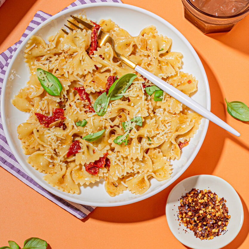 An image of prepared Vegan Sun Dried Tomato Cream Pasta made with farfalle, onion, sun-dried tomatoes, Pacific Foods® Hemp Unsweetened Original Beverage and basil.