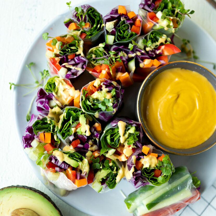 An image of prepared Vegetarian Spring Rolls with Salty Cashew Carrot Ginger Dipping Sauce made with Pacific Foods® Organic Cashew Carrot Ginger Soup, peanut butter, rice paper wrappers, lettuce, cabbage, basil, cilantro, mint, carrots, cucumber, red bell pepper and avocado.