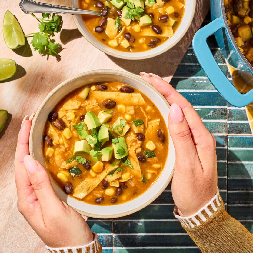 An image of prepared Weeknight Tortilla Soup made with onion, zucchini, corn, black beans, Pacific Foods® Organic Low Sodium Vegetable Broth, Pacific Foods® Organic Creamy Tomato Soup tortillas and avocado.