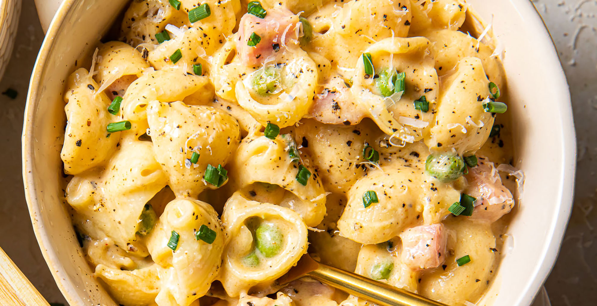 An image of prepared Creamy Stovetop Mac and Cheese with Ham and Peas made with Pacific Foods® Organic Salted Chicken Bone Broth, pasta, peas, evaporated milk, mascarpone, white Cheddar, pepper Jack cheese and ham.