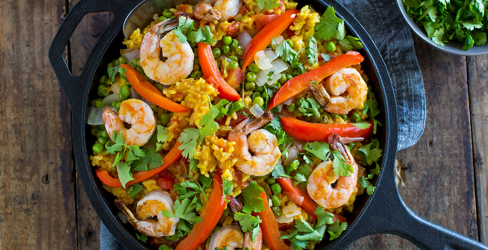 An image of prepared Easy Shrimp and Vegetable Paella made with Pacific Foods® Organic Vegetable Broth, saffron, shrimp, onion, bell pepper, white rice, tomatoes, peas and parsley.