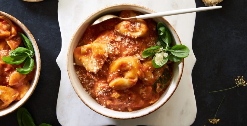 An image of prepared Easy Cheese Tortellini Soup made with onion, bell pepper, sun-dried tomatoes, Pacific Food® Organic Free Range Chicken Broth, crushed tomatoes, basil, cheese tortellini and spinach.
