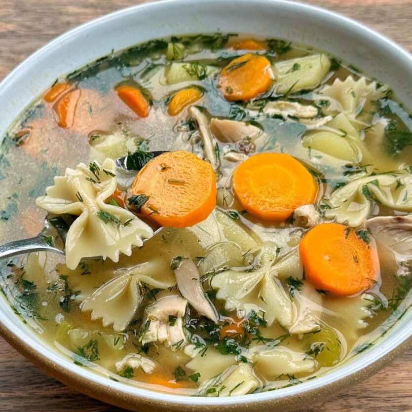 An image of prepared Jake Cohen 30-Minute Chicken Noodle Soup made with Pacific Foods® Organic Free Range Chicken Broth, thyme, onion, carrots, parsnips, celery, rotisserie chicken and bowtie pasta.