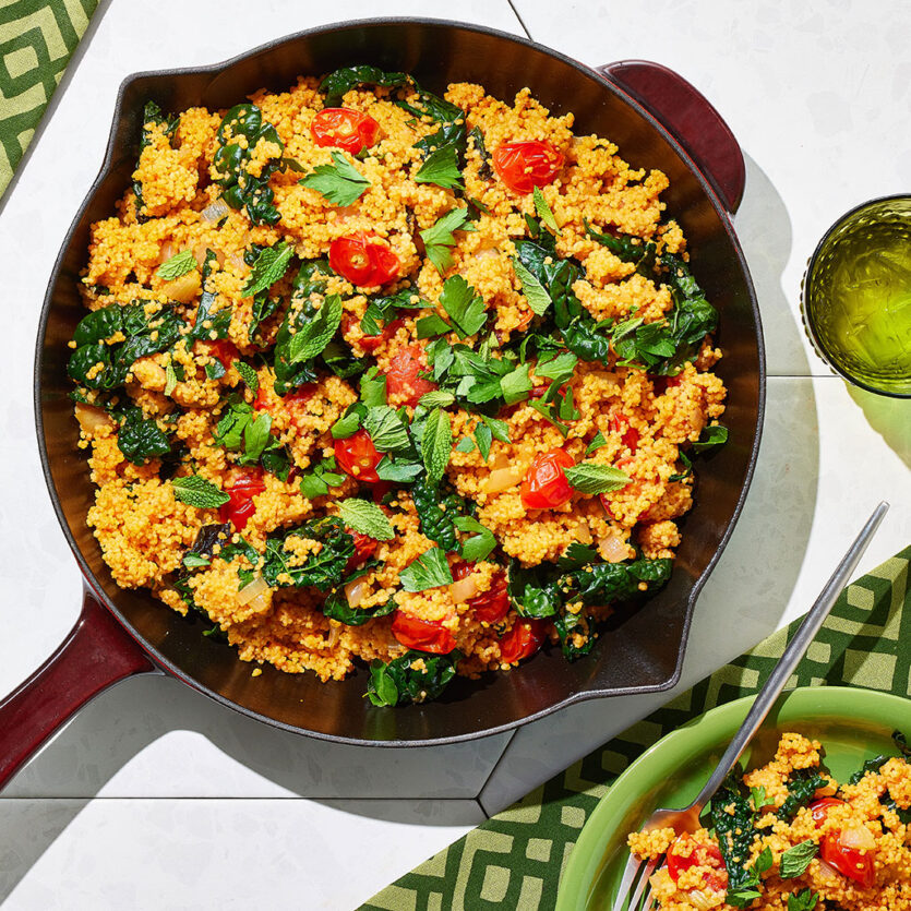 An image of prepared Roasted Red Pepper Couscous with Garlicky Tomatoes, Onions and Kale made with garlic, red bell pepper, Pacific Foods® Organic Low Sodium Vegetable Broth, couscous, Pacific Foods® Organic Roasted Red Pepper & Tomato Soup, grape tomatoes, kale, parsley and mint.