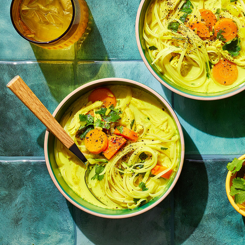 An image of prepared Turmeric Chicken Noodle Soup made with onion, carrots, ginger, garlic, Pacific Foods® Organic Chicken Bone Broth, rotisserie chicken, coconut milk, turmeric, rice noodles, lime juice and cilantro.