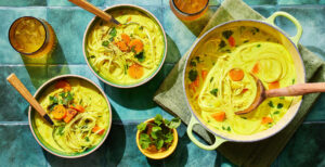 An image of prepared Turmeric Chicken Noodle Soup made with onion, carrots, ginger, garlic, Pacific Foods® Organic Chicken Bone Broth, rotisserie chicken, coconut milk, turmeric, rice noodles, lime juice and cilantro.