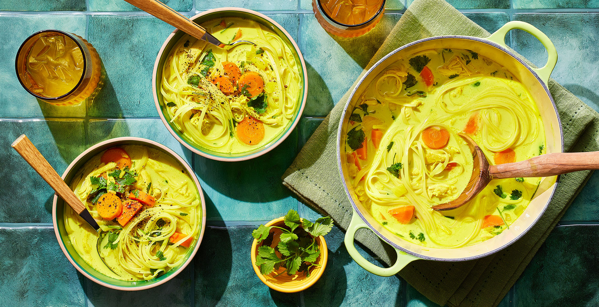 An image of prepared Turmeric Chicken Noodle Soup made with onion, carrots, ginger, garlic, Pacific Foods® Organic Chicken Bone Broth, rotisserie chicken, coconut milk, turmeric, rice noodles, lime juice and cilantro.