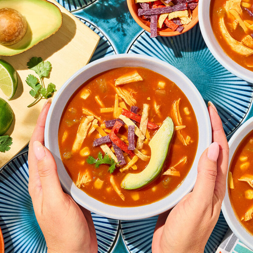 An image of prepared Chicken Enchilada Soup made with Pacific Foods® Organic Condensed Tomato Soup, Pacific Foods® Organic Low Sodium Free Range Chicken Broth, corn, green chiles, chicken, tortilla strips, Cheddar cheese, avocado and cilantro.