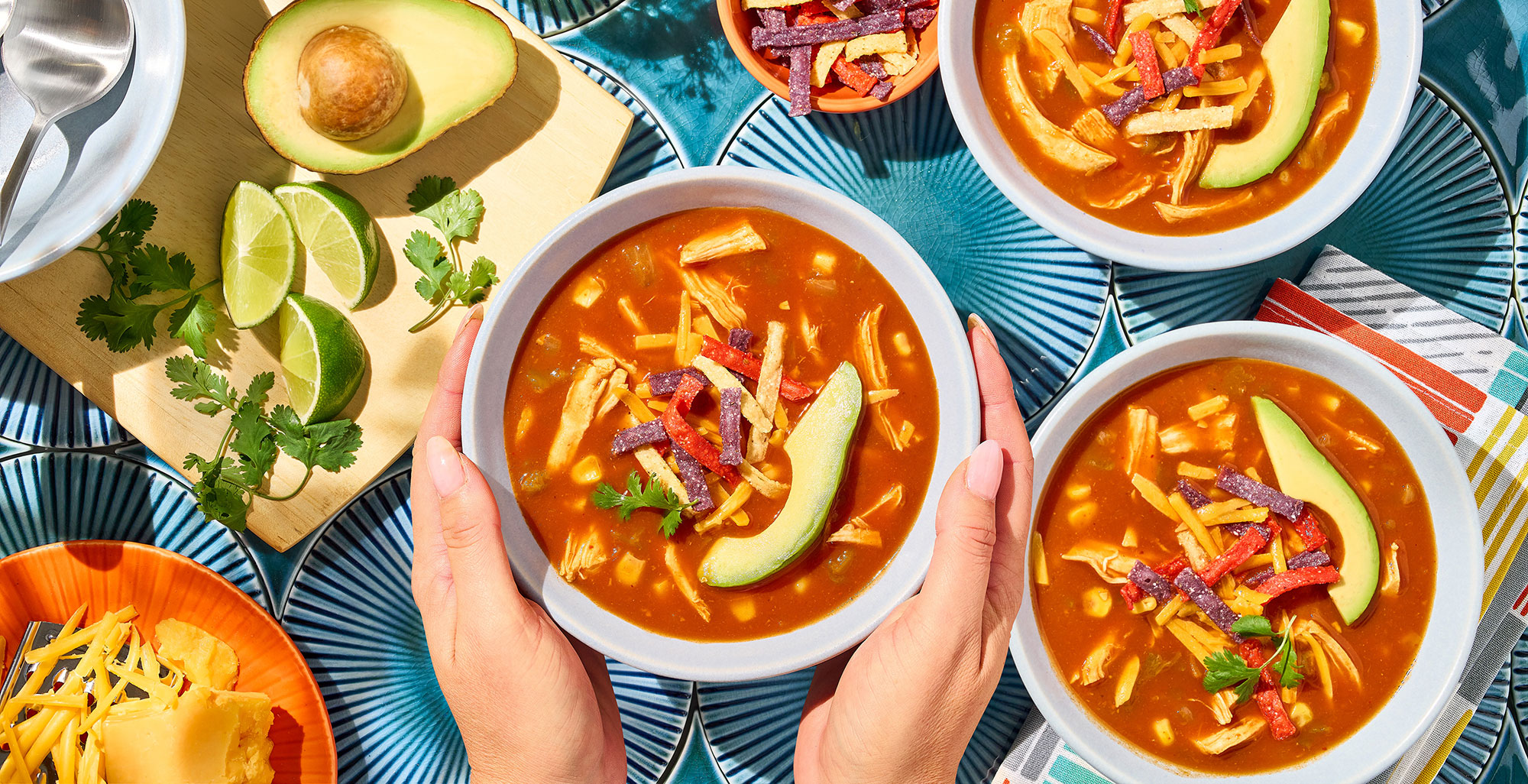 An image of prepared Chicken Enchilada Soup made with Pacific Foods® Organic Condensed Tomato Soup, Pacific Foods® Organic Low Sodium Free Range Chicken Broth, corn, green chiles, chicken, tortilla strips, Cheddar cheese, avocado and cilantro.