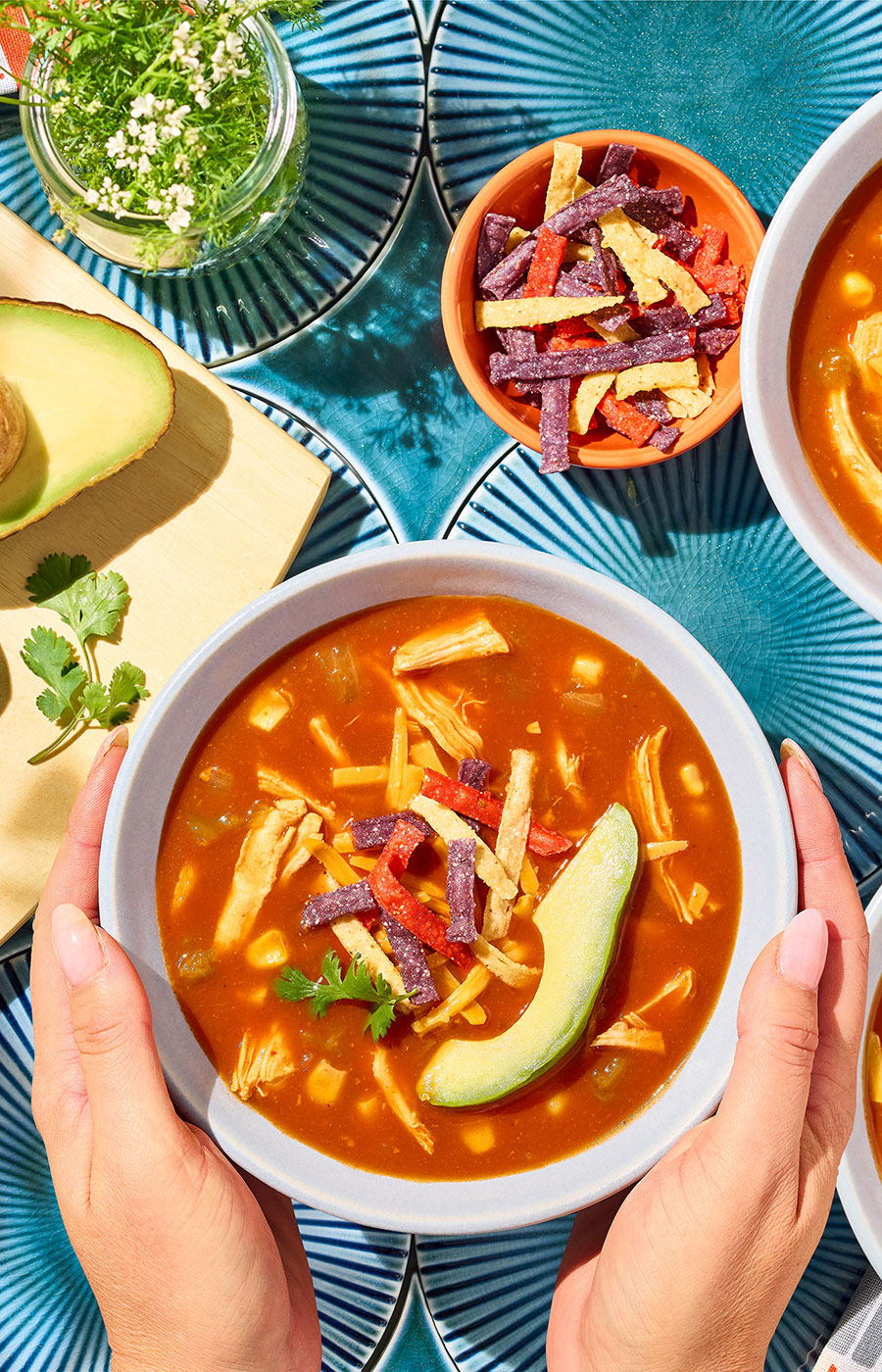 An image of prepared Chicken Enchilada Soup made with Pacific Foods® Organic Condensed Tomato Soup, Pacific Foods® Organic Low Sodium Free Range Chicken Broth, corn, green chiles, chicken, tortilla strips, Cheddar cheese, avocado and cilantro.