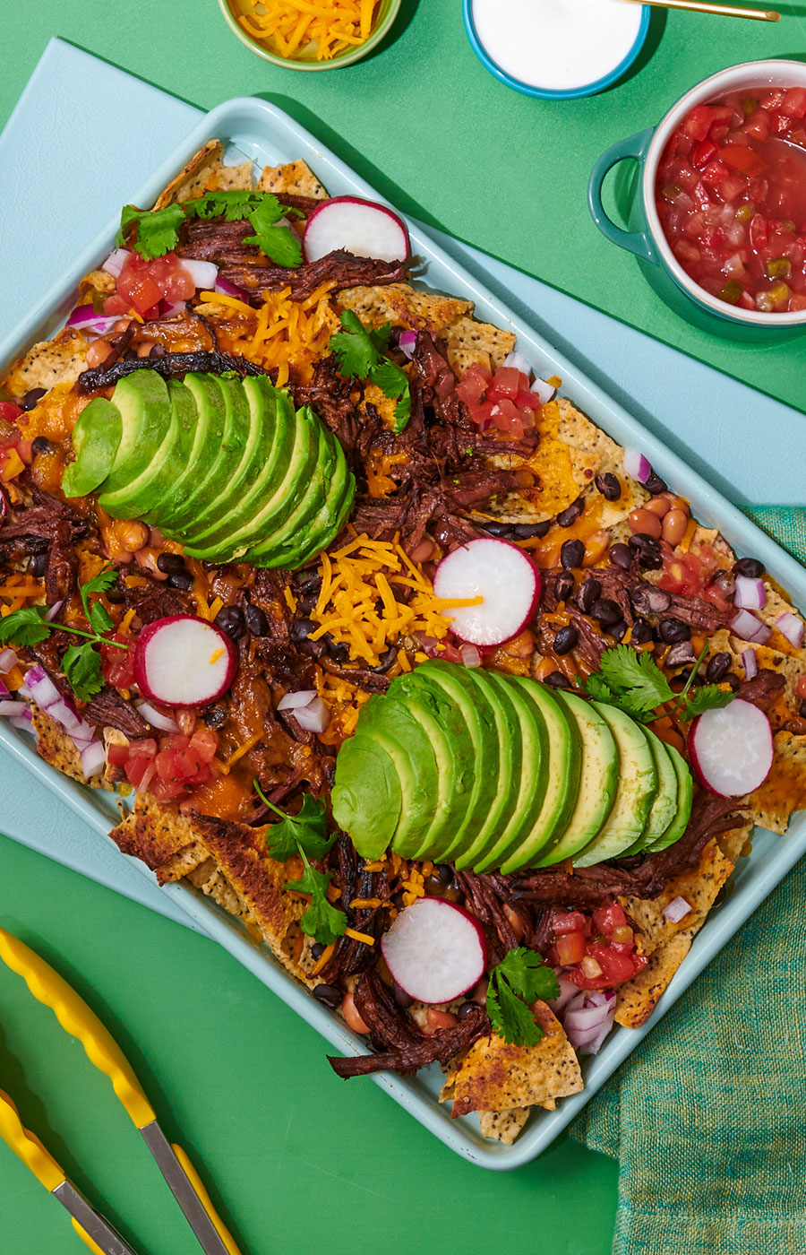 An image of prepared Instant Pot® Shredded Beef Nachos made with Pacific Foods® Organic Beef Broth, chuck roast, tortilla chips, red onion, Cheddar cheese, pico de gallo, black beans, pinto beans, cilantro, radish and avocado.